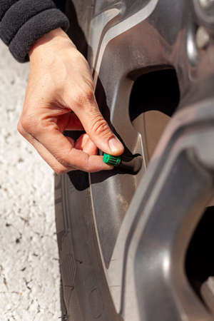 A caucasian woman is removing or attaching the green tire stem valve cap of her vehicle. This is done for checking the tire pressure and inflating when neccessary.の写真素材
