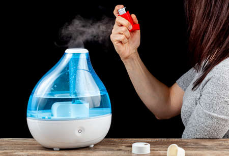 Asthma, allergy attack concept with ultrasonic air humidifier creating cool mist and a woman holding...