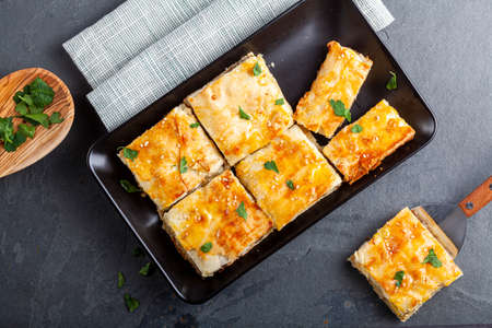 Turkish kiymali borek served on a tray after being sliced into square shapes. Fresh parsley leaves...