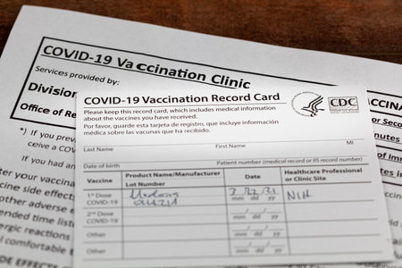 Bethesda, MD, USA 03-22-2021: a COVID 19 vaccination record card on a wooden desk. The card details...