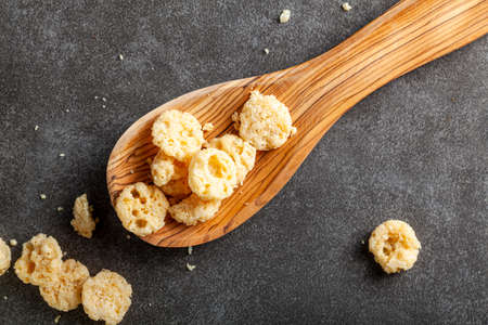 Oven baked cheese bites in a wooden spoon against dark background. These crunchy delicious snacks...