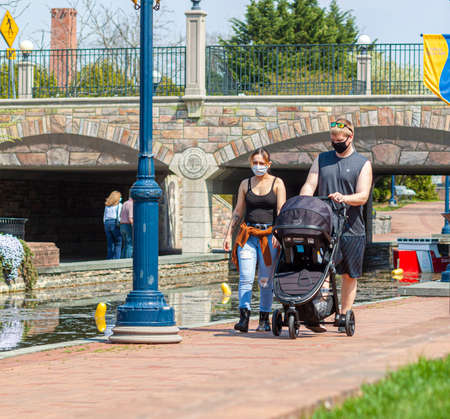 Frederick, MD, USA 04-07-2021: A young caucasian couple is walking in the park with their newborn child inside a stroller. New parents are taking precaution wearing face masks due to COVID-19 pandemicのeditorial素材