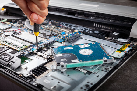 A computer technician is repairing an old laptop using a screw driver. Closeup isolated image showing complex interior of a laptop with circuit boards and delicate items. The person removes a screw.の写真素材