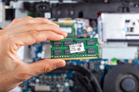 Close up isolated image showing an it technician or a consumer holding ram card in hand with an open laptop interior seen in the background. Concept image for upgrade and repair of electronics.の写真素材