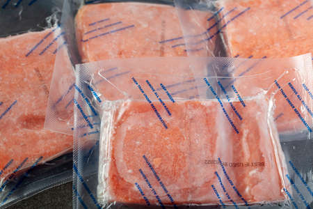 Closeup isolated image of four packs of individually packaged salmon fillets. The air tight vacuum sealed packs are frozen and the instructions say they need to be thawed in fridge.の写真素材