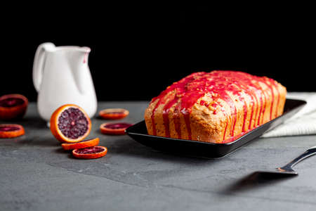 Closeup image of fresh homemade blood orange cake made in a loaf pan and served on black porcelain plate on dark stone background.  It has blood orange juice containing syrup finishing.の写真素材