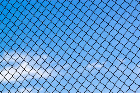 Abstract image showing a latticework of a chain fence covering the entire blue sky. Versatile for concepts like lack of freedom, humanitarian causes, captivity, slavery, limitations, restrictionsの写真素材
