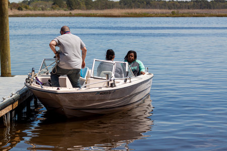 Vienna, MD, 04-16-2021: A Galaxy model small open motorboat with three passengers is setting up for a small trip in Nanticoke river. A man is untying the ropes from dock post by a ramp.のeditorial素材