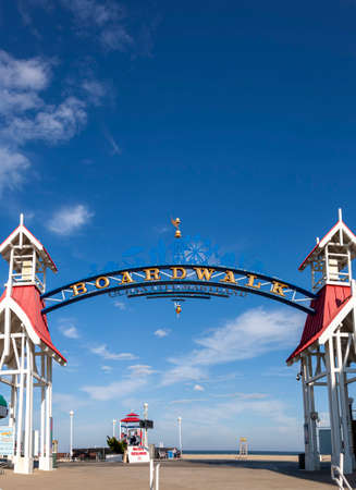 Image  of the entrance of famous board walk by the beach where people are walking on a sunny afternoon. A popular tourist spot on east coast of USA. A wooden arch is erected to mark the spot.の写真素材