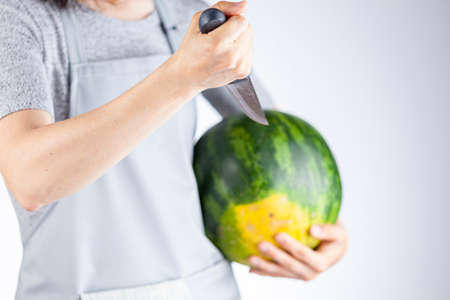 A caucasian woman is preparing to stab a watermelon using a sharp kitchen knife. A versatile image for summer fruits as well as a demonstration of force, metaphorical passive aggressive behaviorの写真素材