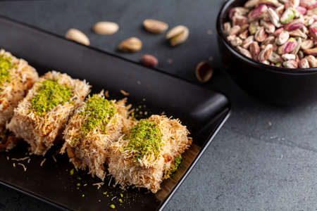 Turkish tel kadayif dessert made from shredded phyllo dough mixed with walnuts. It is sweetened with thick syrup and ground pistachio is added on top for decoration and flavor. A plate with ingredientの写真素材