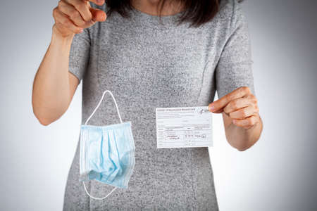 Clarksburg, MD, USA 05-16-2021: CDC announced the lifting of face mask requirement for fully vaccinated individuals. A woman showing vaccination record card is removing her face mask and discarding itのeditorial素材
