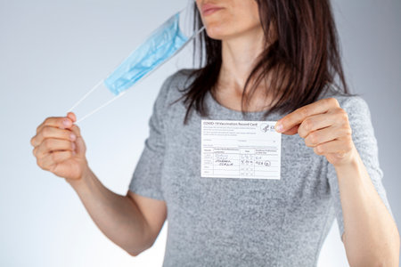 Clarksburg, MD, USA 05-16-2021: CDC announced the lifting of face mask requirement for fully vaccinated individuals. A woman showing vaccination record card is removing her face mask and discarding itのeditorial素材