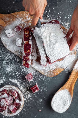 making of delicious fruit flavored homemade Turkish delight with vibrant pink red color and mixed with hazelnuts. Sifted Confectioners sugar is added on top and  dice shaped pieces were cut out.の写真素材
