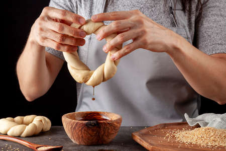 delicious Turkish bagel with sesame seeds known as susamli simit. A woman chef is dipping the rolls into grape molasses to help stick sesamme seeds to the rolled dough.の写真素材