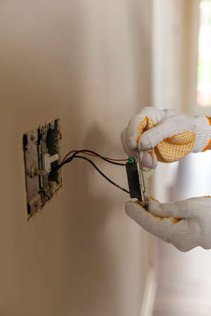 An electrician is replacing a wall switch. A DIY project concept. High voltage danger. The professional is wearing rubber safety gloves for shock prevention. Isolated close up imageの写真素材