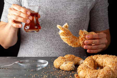 delicious Turkish bagel with sesame seeds known as susamli simit. A woman is eating it together with...