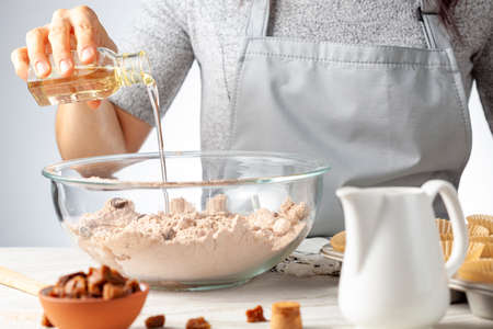 A woman is adding ingredients for making delicious fruit and nut cupcake on white marble countertop...
