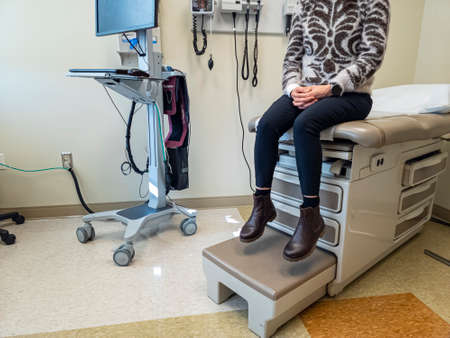 Inside of an  exam room with a bed, some medical devices, a computer. A woman is anxiously waiting for the doctor. Generic image for health care industry, disease, patient and doctor.の写真素材