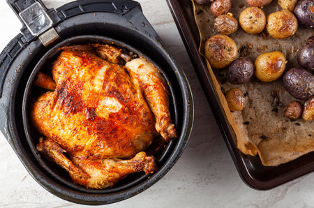 A whole chicken cooked inside an air frier concept. A healthy nutritious homemade alternative to deep fried store bought meat. Served inside the fryers basket together with baked potatoes.の写真素材