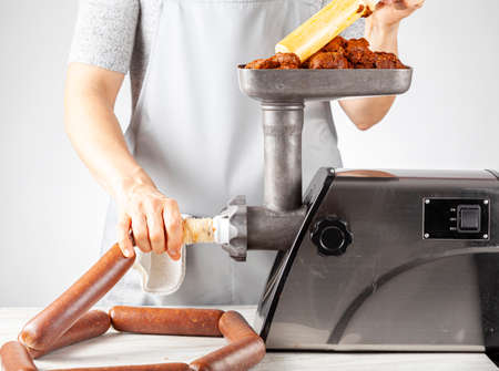 a woman cook wearing apron is stuffing homemade sucuk or sausage into casing using an electrical meat grinder and stuffer. This is an healthier preservative free alternative for these delicious food.の写真素材