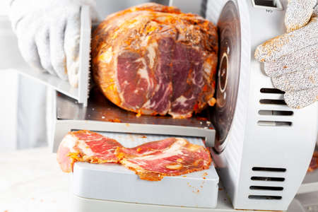 Close up isolated image showing a butcher or chef slicing a large frozen cured meat block. Turkish pastirma, pastrami, ham, beef concept. The person wears protective cut resistant glovesの写真素材