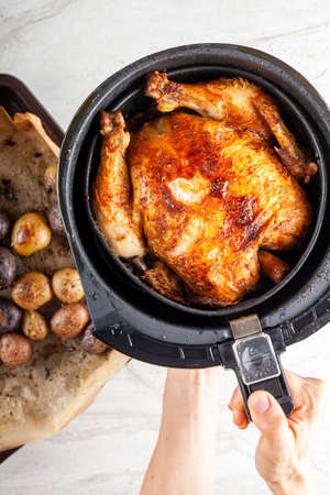 A whole chicken cooked inside an air frier concept. A healthy nutritious homemade alternative to deep fried store bought meat. Served inside the fryers basket together with baked potatoes.の写真素材