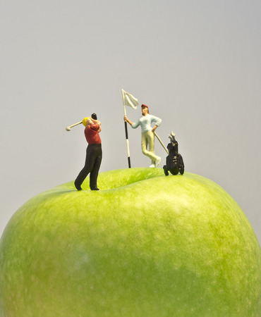 Miniature golf on apple  Macro shot of golfing figurines playing round on top of green appleの写真素材