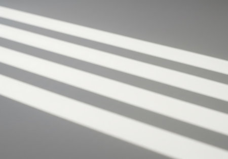 Diagonal lines of light and shadow create an abstract pattern on a plain gray background, suggesting a window or blinds.の素材