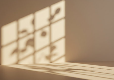 Soft, warm sunlight casts a grid of geometric shadows and light patterns across a neutral, textured wall and floor.の素材