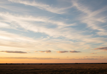 A serene landscape featuring a vast expanse of sky painted with soft, wispy clouds during a gentle sunset over a darkened field.の素材
