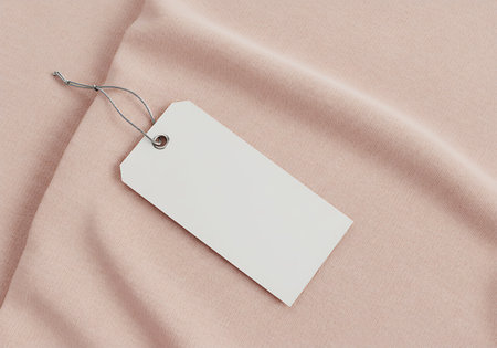 A simple white rectangular tag with a string lies on a textured pink textile surface.の素材