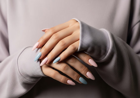 Close-up of hands with beautifully manicured almond shaped nails featuring pastel blue, pink, and white designs.の素材