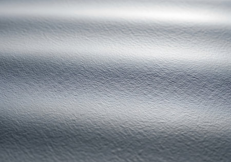 A close-up view of a brushed metal surface with soft, horizontal light reflections creating a textured, metallic background.の素材
