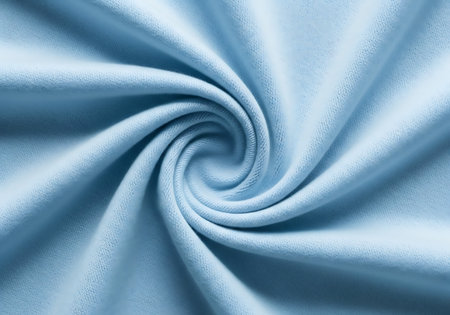 A detailed, close-up view of a soft, light blue fabric creating a swirling pattern with gentle folds and shadows.の素材