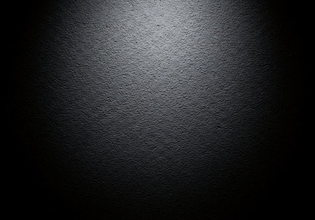A dark textured surface illuminated by a central spotlight, creating a dramatic and moody atmosphere.の素材