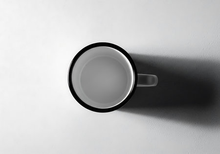 A minimalist black and white photograph of a white ceramic mug viewed from directly above, casting a distinct shadow.の素材