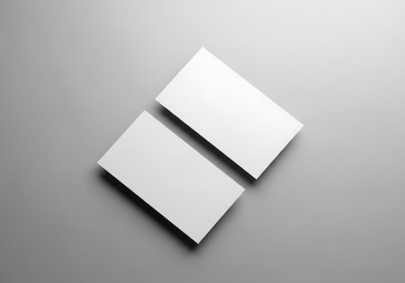 A clean, top-down view of two empty white business cards arranged diagonally on a smooth gray surface.の素材