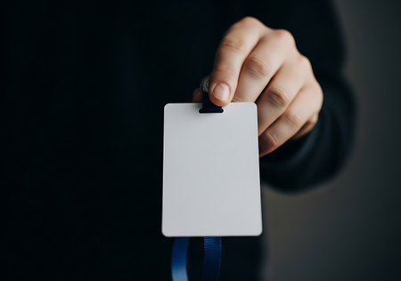 A person's hand displays a blank white identification card, suggesting access or membership. The background is a deep, dark color.の素材