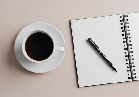 A simple composition featuring a white coffee cup and saucer next to an open spiral-bound notebook and a pen, laid flat.の素材