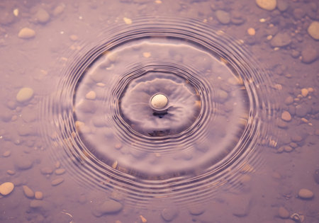 A single water droplet impacts a puddle, generating beautiful, expanding concentric circles of waves. Close-up view.の素材