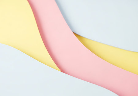 Gentle curves of pastel pink and yellow paper create a minimalist, abstract background with soft shadows.の素材
