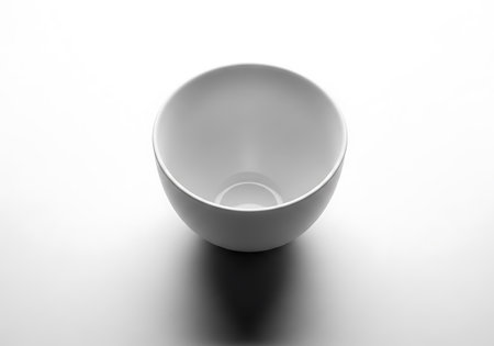 A simple white ceramic bowl is presented from a top-down perspective, casting a subtle shadow.の素材