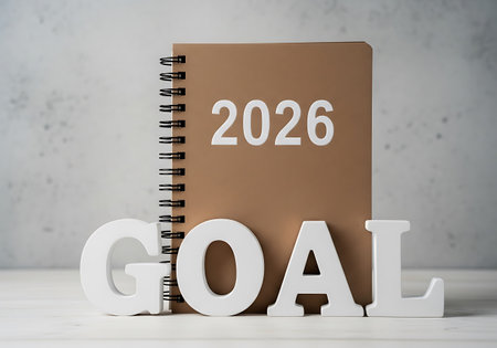 A brown spiral-bound notebook labeled '2026' stands behind large white wooden letters spelling 'GOAL'.の素材