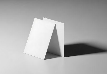 Three blank white cards are arranged in a lean-to formation, casting a strong shadow on a light gray surface.の素材