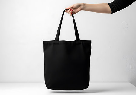 A person's hand holds a simple black canvas tote bag. The bag is empty and hangs vertically.の素材