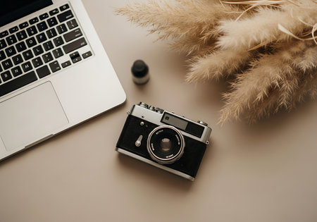 A flat lay of a modern laptop, a classic film camera, and fluffy dried pampas grass, creating an aesthetic workspace.の素材