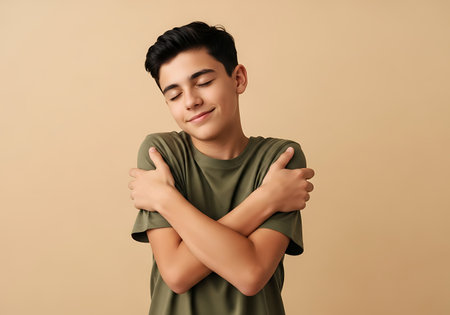 A teenage boy with dark hair and a green t-shirt embraces himself, eyes closed, with a peaceful expression on his face.の素材