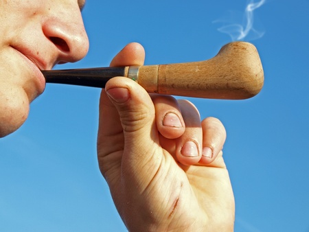 Somebody smoking wooden pipe on sky background        の写真素材