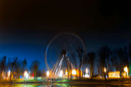 Ferris wheel in a night park on long exposure, reflection in waterの写真素材